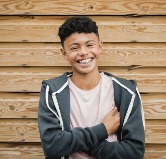 Headshot of a teenage boy with traditional metal braces standing and smiling
